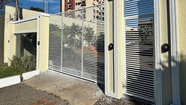 A gated entrance with a metal gate and a door, a concrete pathway, and a tall building in the background. - Ravello Residential AP08 Foz do Iguaçu (Foz do Iguaçu)