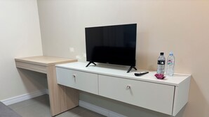 A room with a TV on a white cabinet, a remote, two water bottles, and a grey couch. - Ravello Residential AP08 Foz do Iguaçu (Foz do Iguaçu)