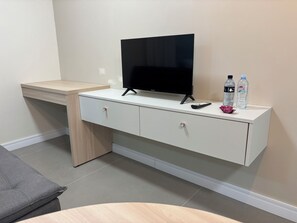 A room with a TV on a white cabinet, a remote, two water bottles, and a grey couch. - Ravello Residential AP08 Foz do Iguaçu (Foz do Iguaçu)