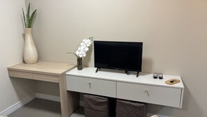 A modern desk with a flat-screen TV, a vase with white flowers, and a potted plant. - Ravello Residential AP08 Foz do Iguaçu (Foz do Iguaçu)