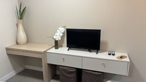 A modern desk with a flat-screen TV, a vase with white flowers, and a potted plant. - Ravello Residential AP08 Foz do Iguaçu (Foz do Iguaçu)