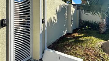 Fachada residencial com porta branca, janela com persianas, luminária na parede e uma palmeira.
