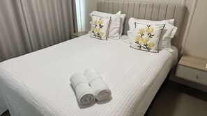 A neatly made bed with two pillows and two rolled towels, a bedside table, and a nightstand. - Ravello Residential AP08 Foz do Iguaçu (Foz do Iguaçu)