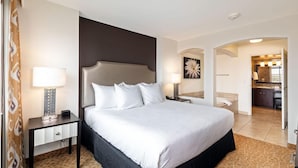 Hotellihuone, jossa on suuri sänky, yöpöytä lampun kanssa, pieni sivupöytä, kylpyhuone, joka näkyy holvikaaren läpi, ja pieni keittotila.