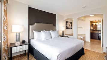A hotel room with a large bed, a bedside table with a lamp, a nightstand, a bathroom visible through an archway, and a kitchenette area.