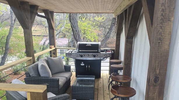 En täckt uteplats med en grill, möbler i rotting och en barstol.