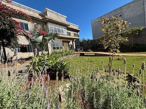 Un edificio con un giardino antistante, un muro in pietra e un cielo azzurro limpido.