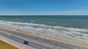A coastal road with a beach on one side and a clear blue sky. - Ocean Grove 1003 - Pelican Sky (Galveston)