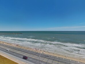 A coastal road with a beach on one side and a clear blue sky. - Ocean Grove 1003 - Pelican Sky (Galveston)