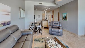 A living room with a leather sofa, a dining table with chairs, a leather recliner, and a tray of seashells. - Ocean Grove 1003 - Pelican Sky (Galveston)