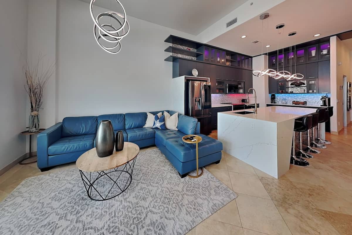 A modern living room with a blue sofa, a coffee table, and a kitchen area with a bar.