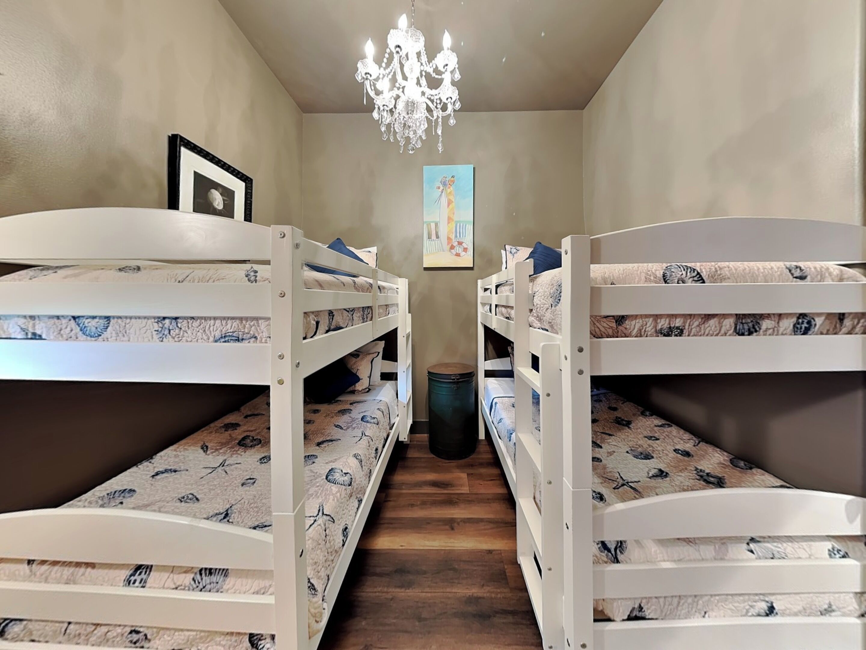 A bunk room with two bunk beds, a chandelier, a picture on the wall, and a trash can.