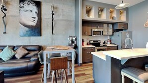 A modern kitchen with a central island, a dining area with a table and chairs, and a living room with a sofa and a large painting. - Ocean Grove PH 1101 - The Sky Gallery Penthouse (Galveston)