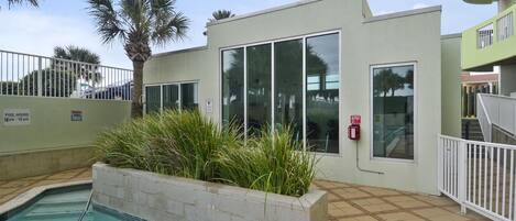 A pool area with a 3 ft 6 in depth, surrounded by a low wall and plants, with a building featuring large windows and a fire alarm.