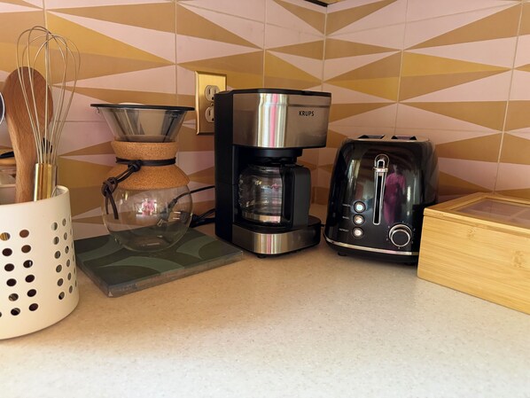 Uma bancada de cozinha com uma cafeteira, torradeira e um recipiente com batedores.