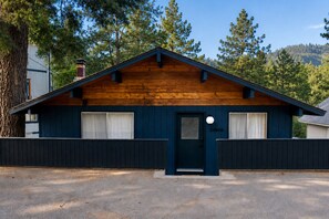 A single-story building with a dark blue exterior, a wooden gable roof, and a small front porch. - Jewel - 1960s Design Cabin • Walk to Lake Gregory (Crestline)