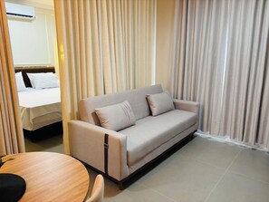 A hotel room with a sofa, a bed, a round wooden table, and curtains. - Ravello Residencial – Comfort and tranquility in Foz do Iguaçu (Foz do Iguaçu)