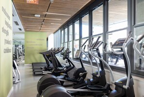 Ein Fitnessstudio mit Laufbändern, Crosstrainern und Ergometer, großen Fenstern und motivierenden Wandbildern.