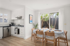 A modern kitchen with white cabinetry, a dishwasher, and a dining area with a table set for four.