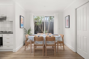 A dining area with a table set for four, surrounded by wooden chairs, in a room with white walls and a large window.