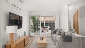 A modern living room with a sofa, coffee table, TV, and a view of the outside.