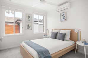 A bedroom with a bed, bedside tables, a ceiling fan, and artwork on the wall.