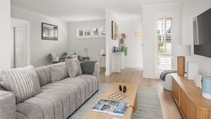 Een moderne woonkamer met een grijze bank, een salontafel met een tijdschrift, een televisie en een houten bijzettafeltje.