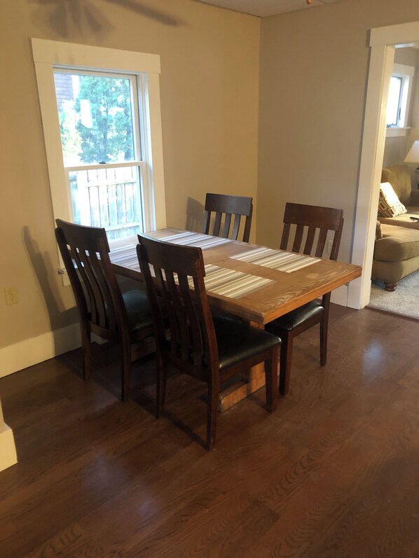A dining table with four chairs, a window, and a door leading to another room.