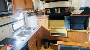 Cocina compacta en una casa rodante, con microondas, fregadero y estufa, un cubo de basura pequeño y un ventilador de techo.