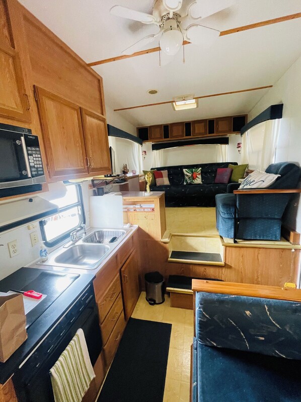 A compact RV kitchen with a microwave, sink, and stove, a small trash can, and a ceiling fan.