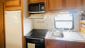 Una cocina compacta con armarios de madera, un microondas, una estufa y un lavamanos.