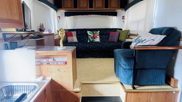 Interior compacto de una autocaravana con kitchenette, zona de estar con cojines y un pequeño cubo de basura.