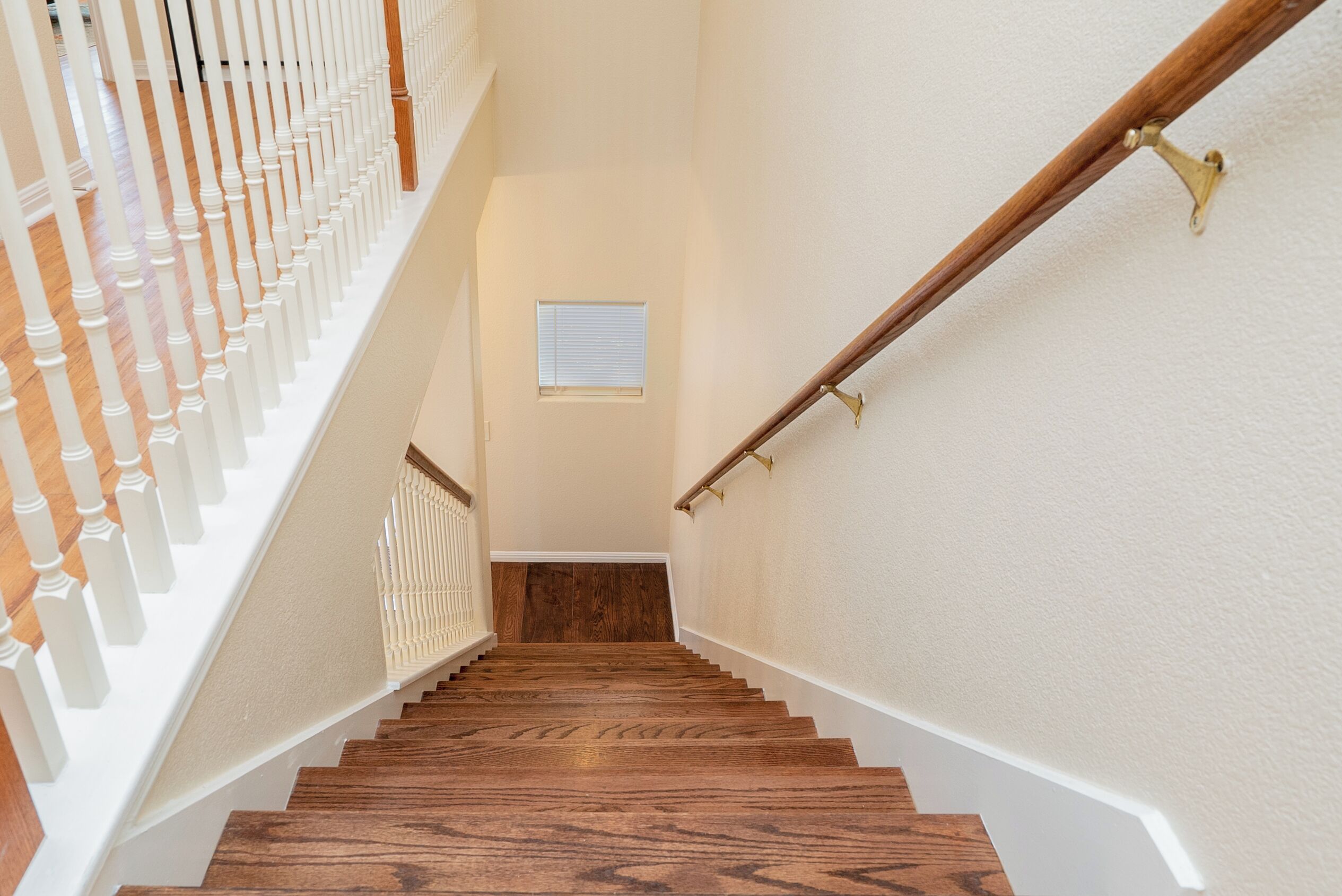 Un escalier en bois, doté de balustrades blanches et d’une main courante, mène à un palier où se trouve une petite fenêtre.