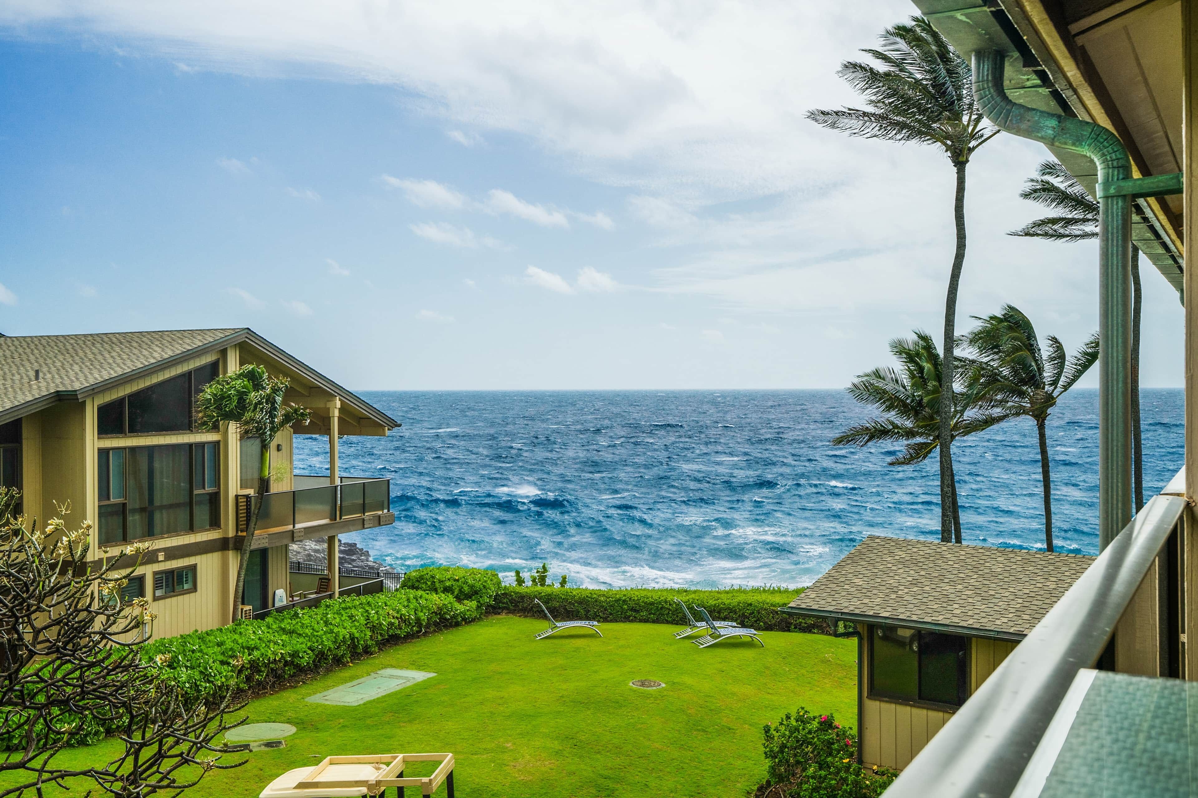 A view of the ocean from a balcony with a lawn and lounge chairs.