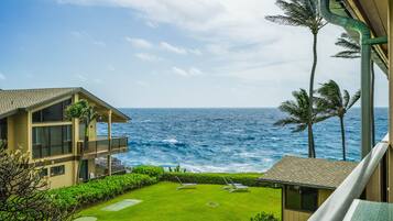 A view of the ocean from a balcony with a lawn and lounge chairs.