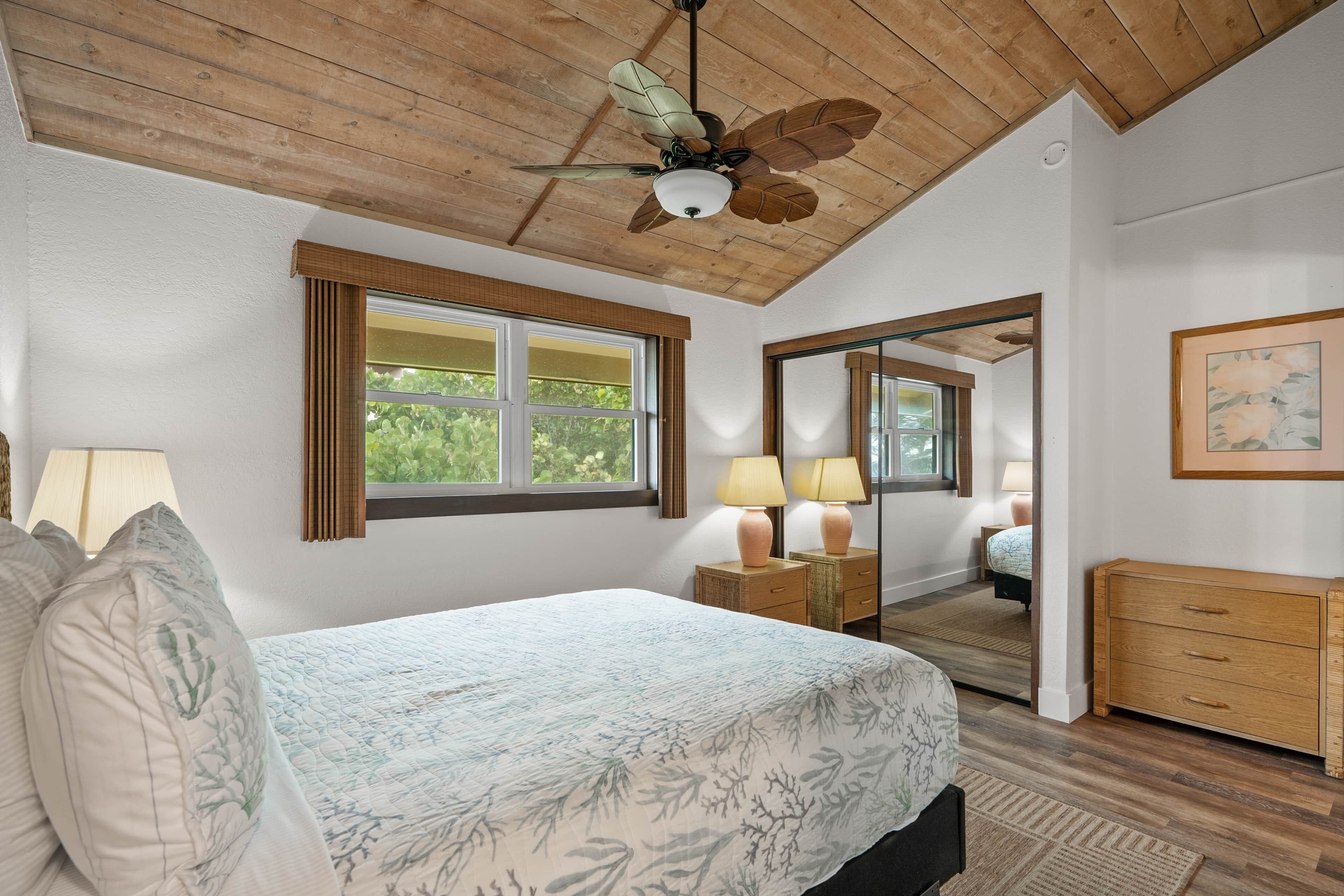 A bedroom with a bed, a ceiling fan, a window, a mirror, a dresser, and a lamp.