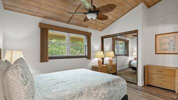 A bedroom with a bed, a ceiling fan, a window, a mirror, a dresser, and a lamp.