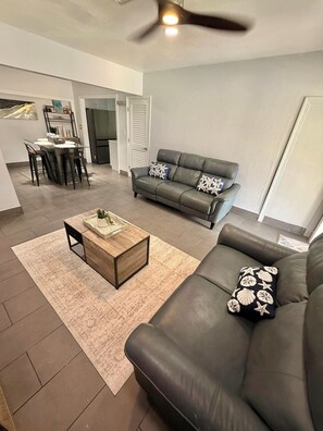 A modern living room with a leather sofa, a wooden coffee table, and a dining area with a kitchen in the background. - Fabulous comfortable house in the heart of Miami. (Miami)