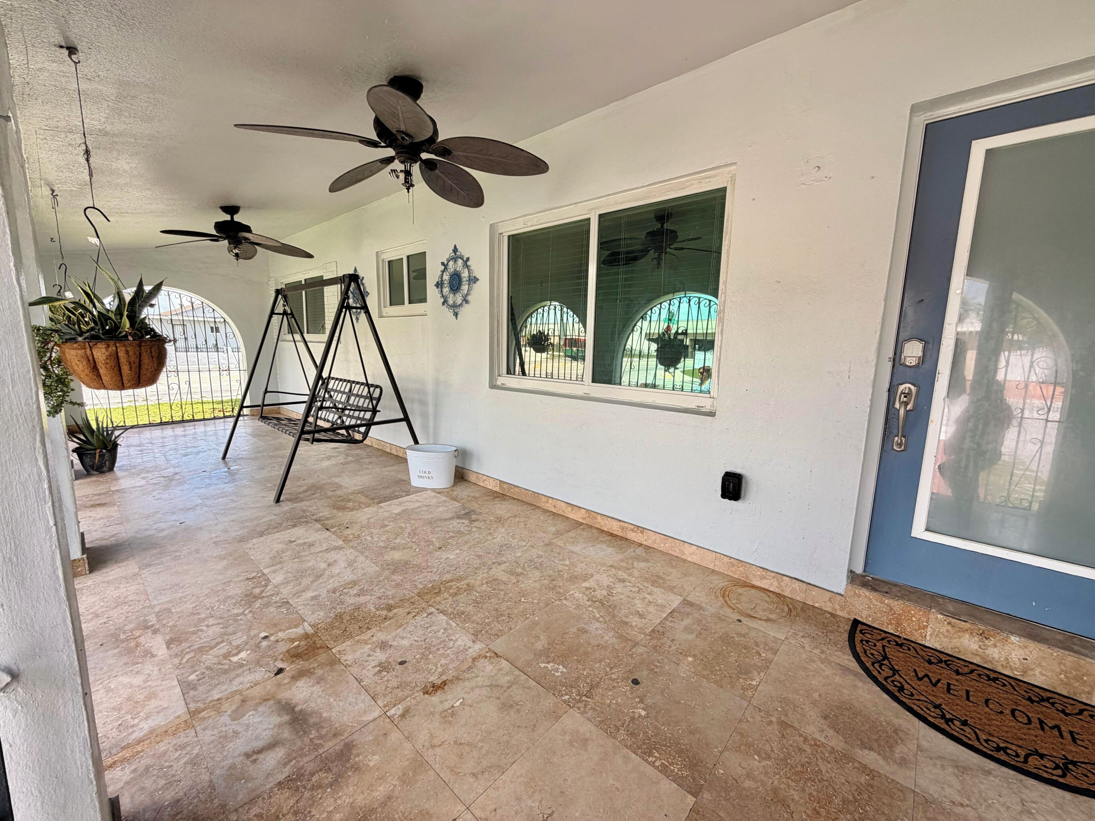 A spacious room with a tiled floor, a ceiling fan, a swing chair, and a welcome mat.
