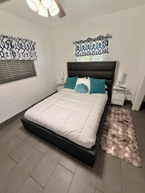 A bedroom with a bed, two bedside tables, a nightstand, a window with blinds, and a patterned curtain. - Fabulous comfortable house in the heart of Miami. (Miami)