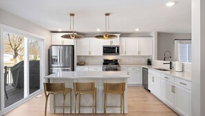 A modern kitchen with white cabinets, stainless steel appliances, and a central island with bar stools. - Private Pool, Infared Sauna, Full Gym, Hot Tub, Sleeps 16 (Grandville)