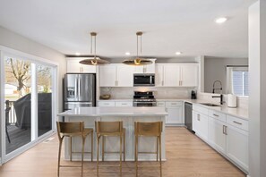 A modern kitchen with white cabinets, stainless steel appliances, and a central island with bar stools. - Private Pool, Infared Sauna, Full Gym, Hot Tub, Sleeps 16 (Grandville)