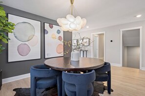 A dining area with a round table, blue chairs, a vase with branches, and abstract wall art. - Private Pool, Infared Sauna, Full Gym, Hot Tub, Sleeps 16 (Grandville)