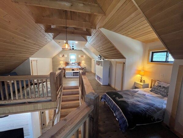 Ein Schlafzimmer im Loftsstil mit einer Holztreppe, einem Bett, einem Schreibtisch und einem Fenster.