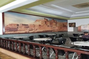 Un restaurante con un mural de un sitio histórico, varias mesas y sillas, y una barandilla de madera.