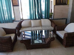 A living room with a glass coffee table, wicker furniture, and a view through large windows.