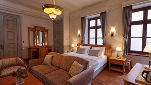 Hotellihuone, jossa on suuri sänky, sohva, puinen yöpöytä, työpöytä, peili ja kattokruunu.