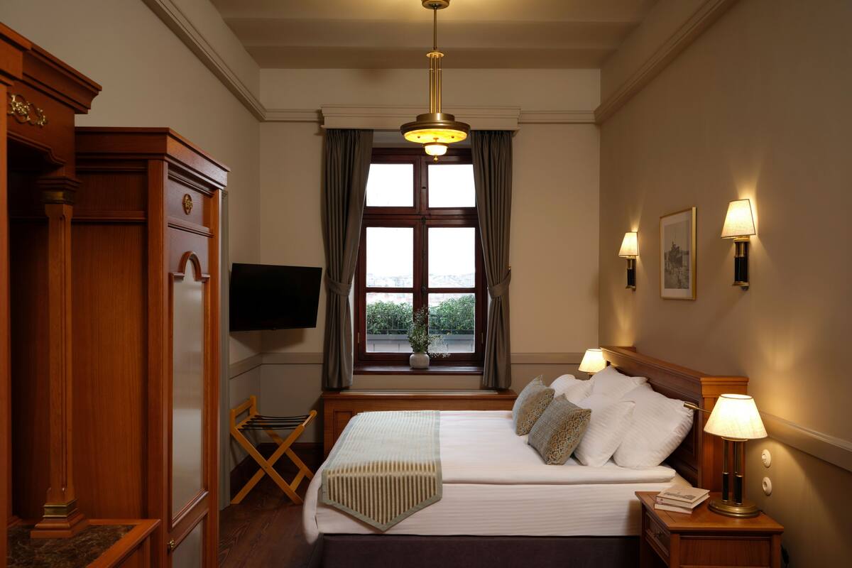A hotel room with a large bed, wooden furniture, a television, a window with curtains, and wall-mounted lamps.