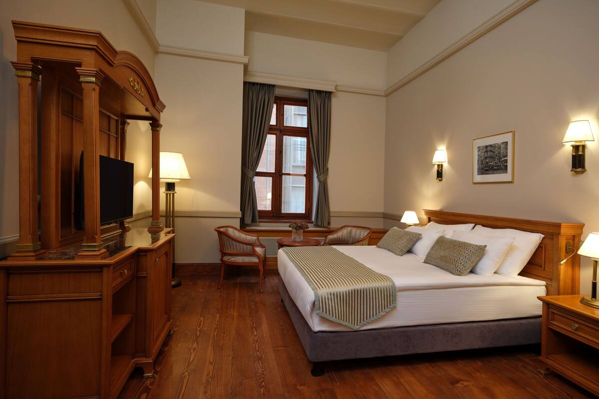 A hotel room with a large bed, a desk, a chair, a television, and a window with curtains.