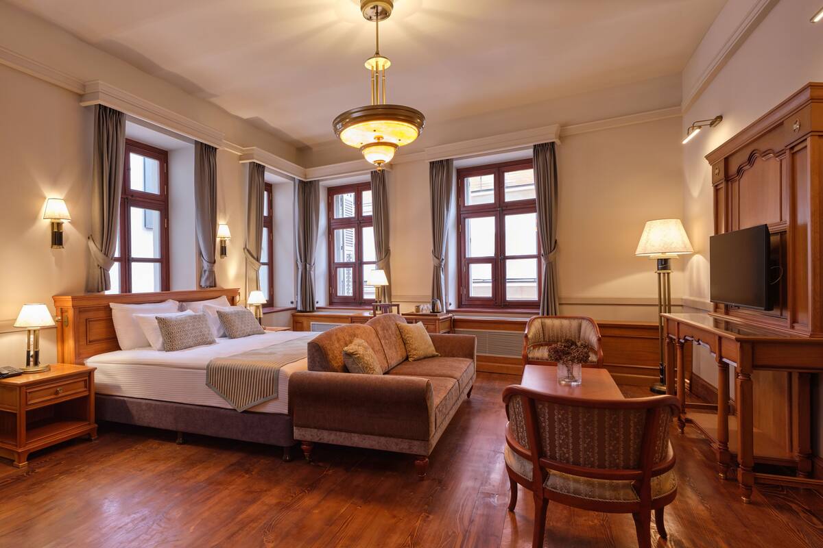 A hotel room with a bed, a sofa, a chair, a TV, and a desk.